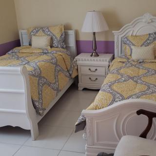 A cozy bedroom featuring two twin beds with matching yellow and gray bedding, separated by a white nightstand with a lamp.