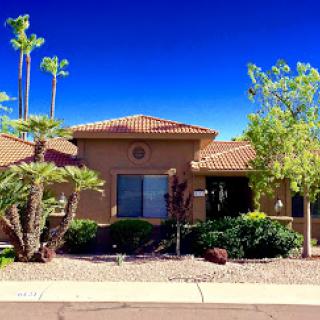 A beautiful single-story house with lush landscaping and palm trees under a clear blue sky.