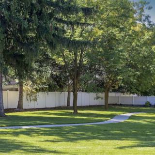 A tranquil garden scene with lush grass, trees, and a white fence basking in sunlight.