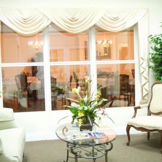 A cozy living room interior featuring elegant curtains, a glass coffee table with a floral arrangement, and comfortable seating.