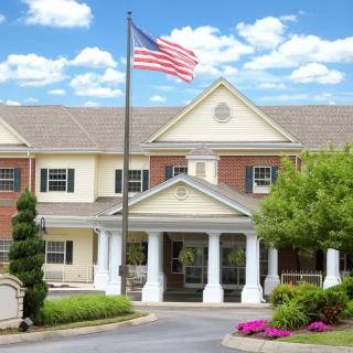 A large building with a prominent entrance and an American flag flying in front, surrounded by landscaping and under a partly cloudy sky.