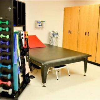 A physical therapy room featuring a therapy table, exercise equipment, and storage cabinets.