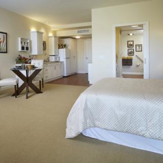 A cozy studio apartment featuring a bedroom area, desk, and kitchenette.