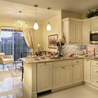 A stylish and modern kitchen with cream-colored cabinets, a decorative backsplash, and elegant lighting fixtures.