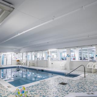 An indoor swimming pool adjacent to a fitness center with exercise equipment.