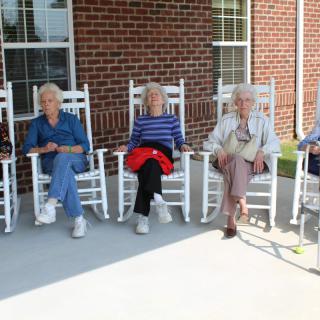 A group of seniors relaxing on rocking chairs on a porch.