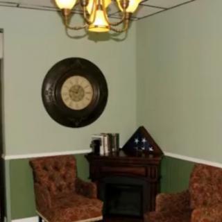 A classic room interior with two chairs, a wall clock, and a small desk beneath a chandelier.