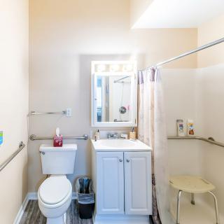 A clean and bright bathroom featuring a sink, toilet, shower with curtain, and a mirror above the white cabinet.