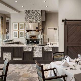 Modern restaurant interior with visible kitchen and elegantly set tables.