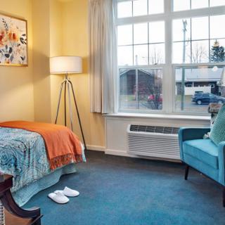 A cozy bedroom with a single bed, blue chair, and large window.