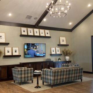 A stylish living room with a modern chandelier, patterned sofas, a mounted television, and decorative artwork on shelves.