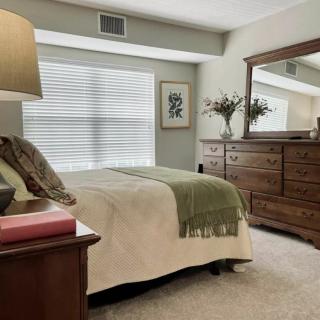 A cozy bedroom with a large bed, wooden dresser, and mirror, creating a warm ambiance.