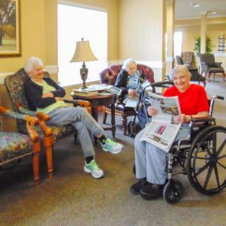 A group of seniors relaxing in a cozy common area, with one reading a newspaper.