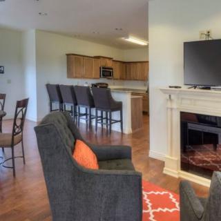 A cozy open floor plan featuring a living room with a fireplace and TV, leading to a kitchen area with bar stools.