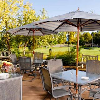A peaceful outdoor patio with tables and umbrellas set in a garden setting on a sunny day.
