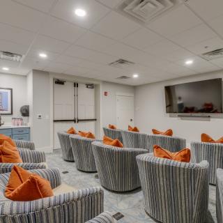 A cozy home theater with striped seating and orange pillows facing a large screen.