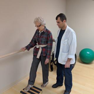 A physiotherapist assists an elderly woman with balance exercises in a rehabilitation session.
