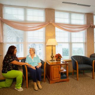 A caregiver interacting with an elderly woman in a cozy room of a care facility.
