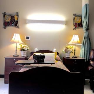 A well-lit hospital room featuring a bed, nightstands with lamps, and artwork on the walls.
