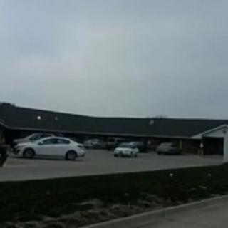 A parking lot with several cars in front of a long, low building under an overcast sky.