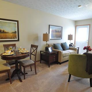A cozy living room with a small dining area featuring a sofa, chairs, and decorative artwork.