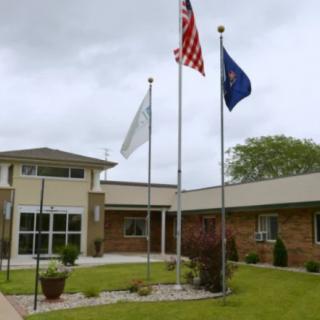A building entrance with three flags flying on a cloudy day.