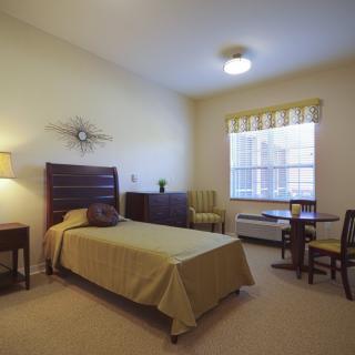 A minimalist bedroom with a single bed, side table, lamp, and window.