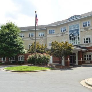 A three-story building with an American flag in front, surrounded by trees and a landscaped entrance.