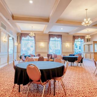 An elegant conference room with round tables and chairs, featuring chandeliers and large windows.