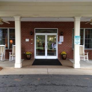 Front entrance of a building with double glass doors and rocking chairs on the porch.
