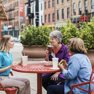 Three women enjoying drinks and conversation at an outdoor cafe in the city.