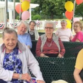 A group of elderly people enjoying an outdoor celebration, surrounded by colorful balloons.