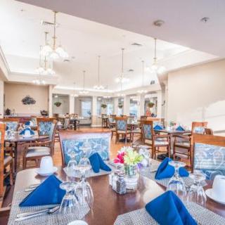 An elegantly set dining room with tables prepared for guests, featuring blue napkins and decorative centerpieces.