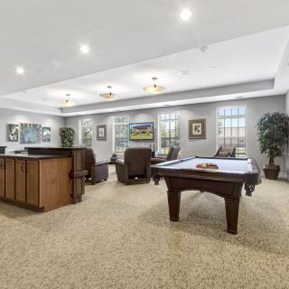 A spacious game room featuring a billiard table, comfortable seating, and decorative artwork on the walls.