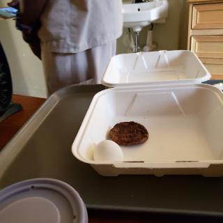 A takeout meal consisting of a small patty and an egg on a tray.