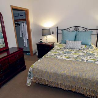 A cozy bedroom with a neatly made bed, bedside lamps, and an open closet.