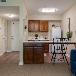 A cozy apartment kitchen with wooden cabinets, a refrigerator, and a seating area.