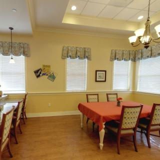 A cozy dining room with neatly arranged tables and chairs, illuminated by a chandelier.