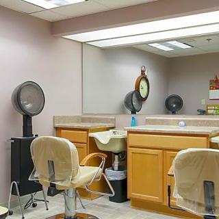 An empty hair salon with mirrored walls, equipped with barber chairs, sinks, and hair dryers.