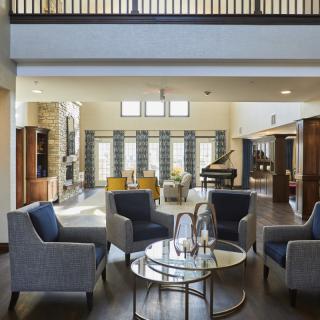 A spacious and modern living room featuring a seating area with comfortable chairs, a glass coffee table, and a grand piano in the background.