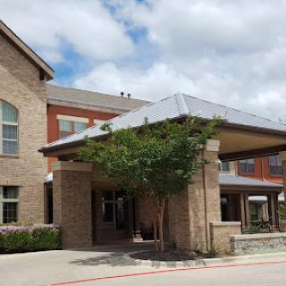 A welcoming entrance to a brick building with a covered area and greenery.