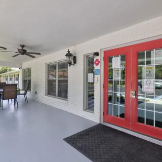 The image shows an outdoor entrance area with red double doors, ceiling fans, and patio seating.