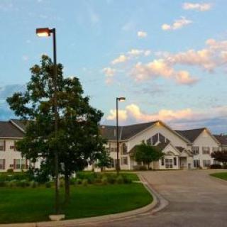 A serene view of a large white building with a tree-lined driveway under a partly cloudy sky.