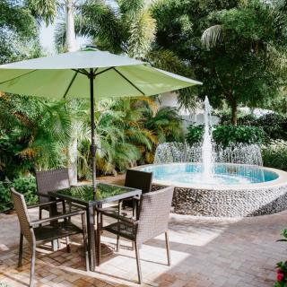 A tranquil patio seating area with a green umbrella and a nearby fountain in a lush garden setting.