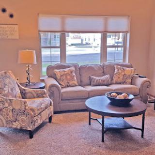 A cozy living room featuring a comfortable sofa, an elegant armchair, and a round coffee table, illuminated by natural light.