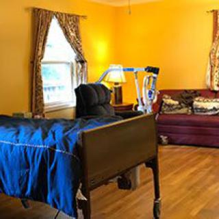 A cozy room with a hospital bed and a sofa, decorated with yellow walls and windows with curtains.