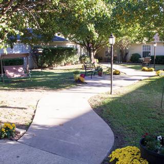 A serene garden path with benches and blooming flowers under the shade of trees.