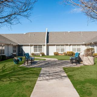 A residential area with a pathway leading to a house, surrounded by well-maintained lawns and outdoor seating.