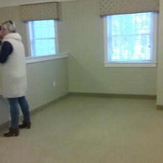 A person stands in an empty room with two windows, showcasing minimal furnishings.