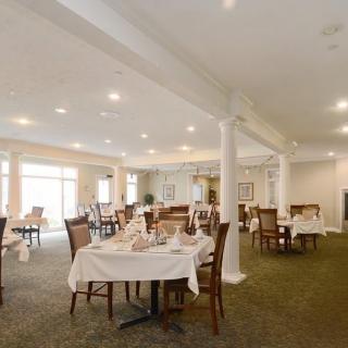 An elegant dining room set up with neatly arranged tables and chairs, featuring white tablecloths and ambient lighting.
